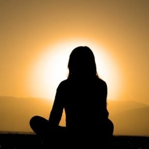 Here's an alt tag for the image: Silhouette of woman meditating at sunset.